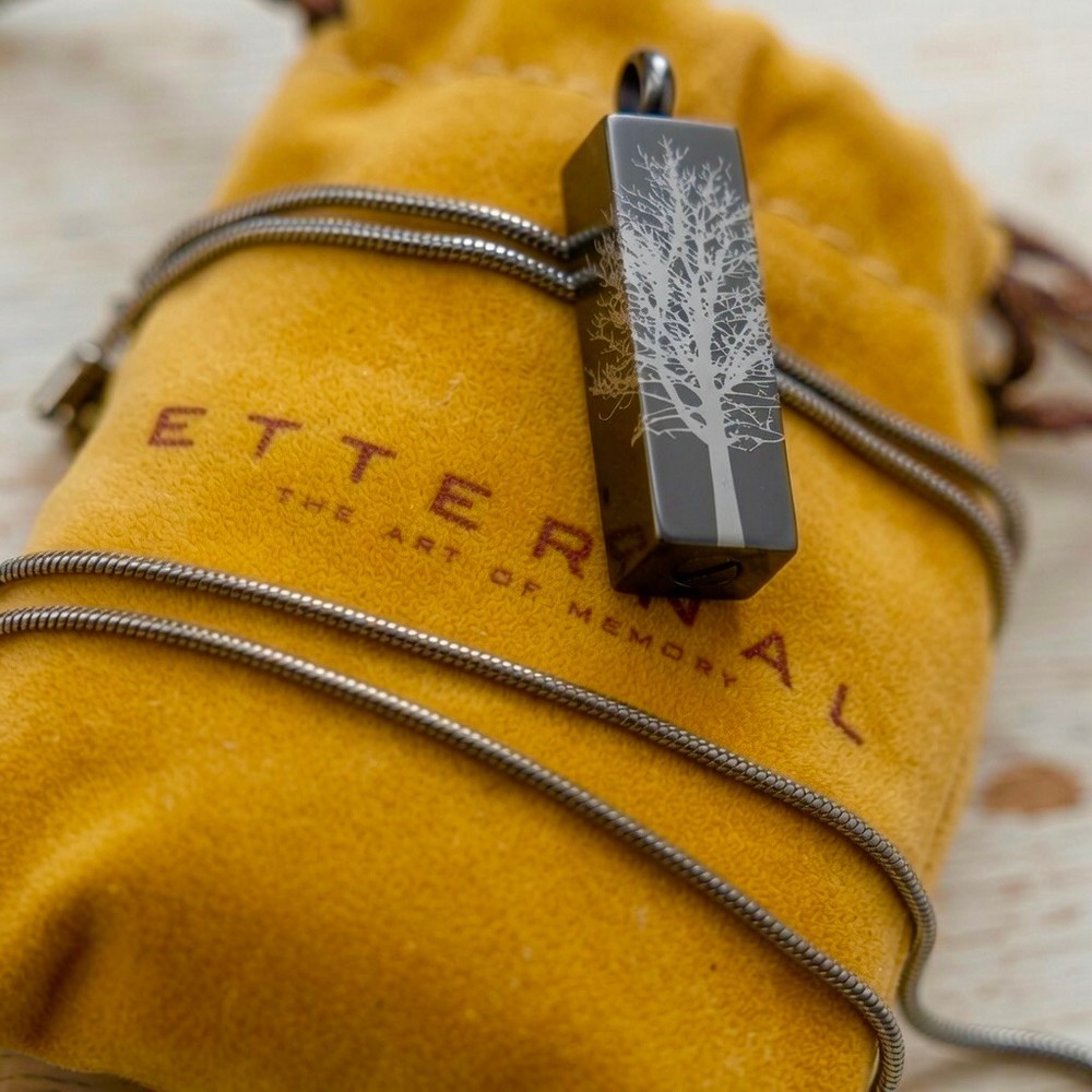 Cremation Jewell Tree Root Graphite Pendant by Etternal on a mustard pouch with the tree root design visible on the rectangular
