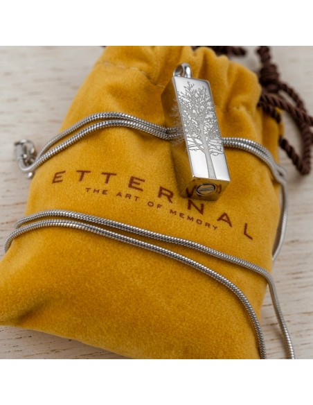 Cremation Jewell Tree Root Pendant on a silver chain rests on a yellow pouch with “ETERNAL” and “THE ART OF MEMORY” text visible
